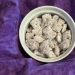 A small white ramekin full of Muddy Buddy snack mix lays atop a dark purple cloth napkin, draped as a background. Photo by Diana Ludwick, copyright 2026.