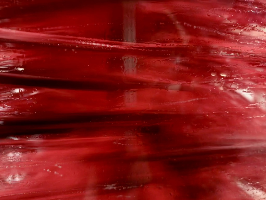 Abstract horizontal streaks of ruby, burgundy, oxblood swirl across a glass panel. Macro action shot of a carwash cleaning curtain flowing across a car window.