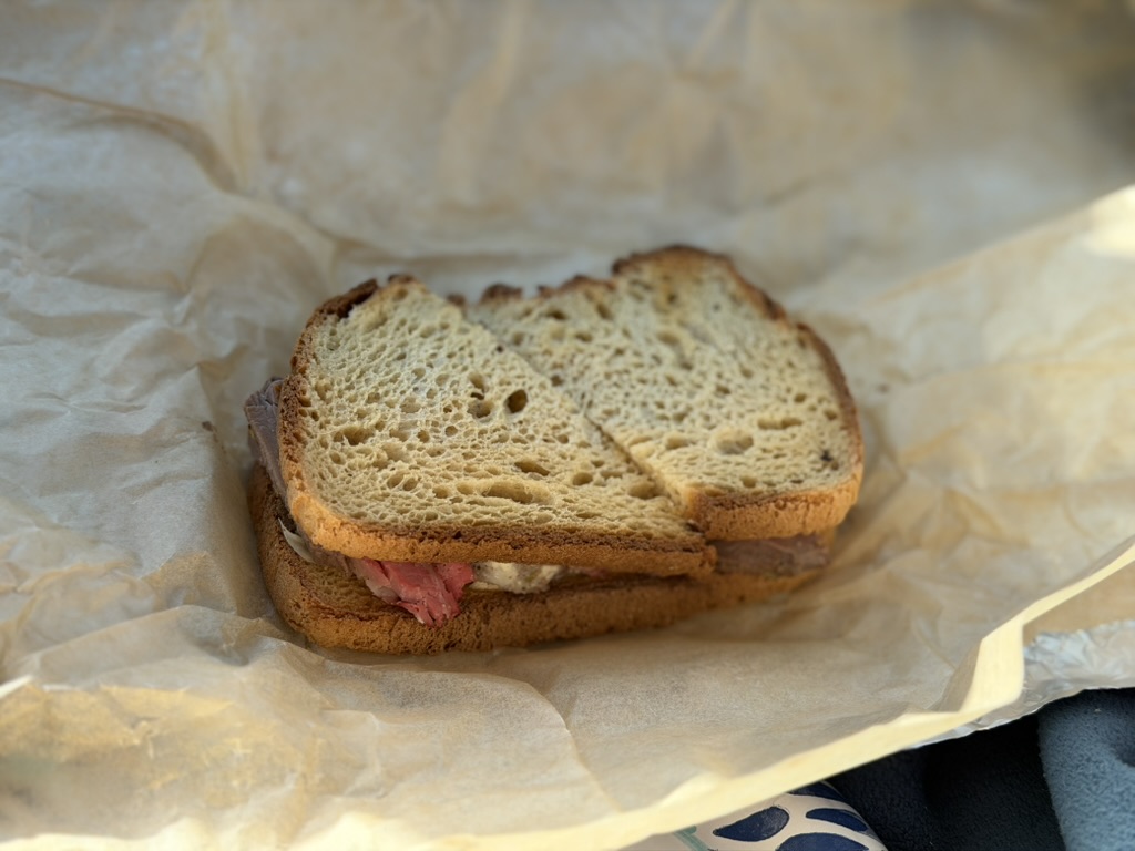Photograph of a steak filet and horseradish sandwich, on the lap of an unseen diner.
