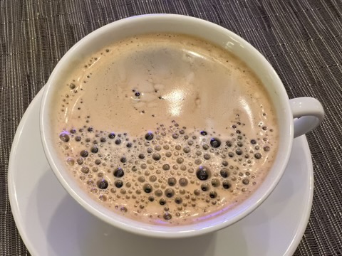 A mug of freshly brewed black coffee with crema bubbles floating at the surface.