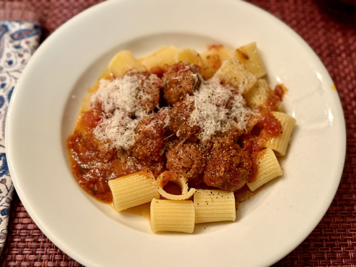 Close-up portrait of Nonna's Sunday gravy, a red sauce with meat, atop wide, short, tubular pasta.