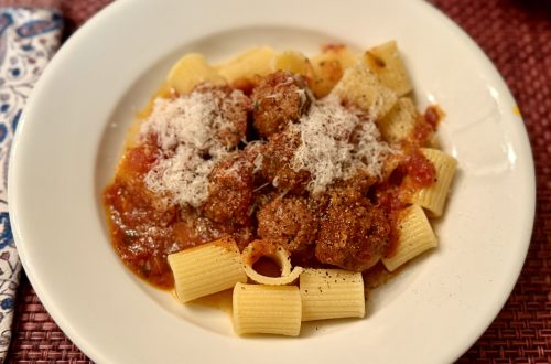 Close-up portrait of Nonna's Sunday gravy, a red sauce with meat, atop wide, short, tubular pasta.